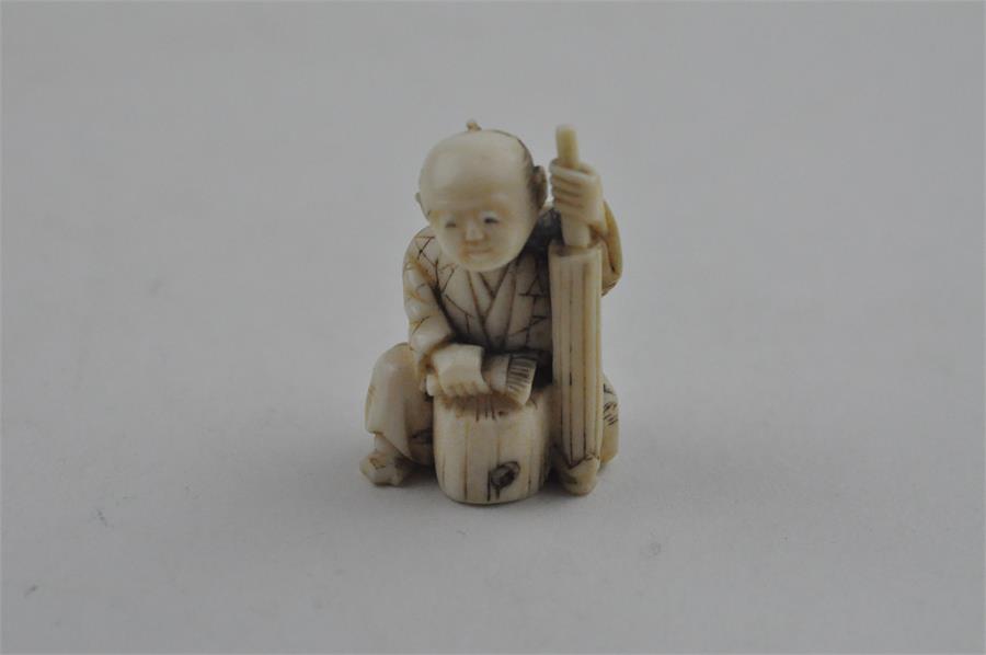 A Japanese late Meiji period carved ivory small okimono, of a man seated by log with a brush. Height