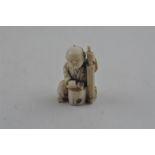 A Japanese late Meiji period carved ivory small okimono, of a man seated by log with a brush. Height