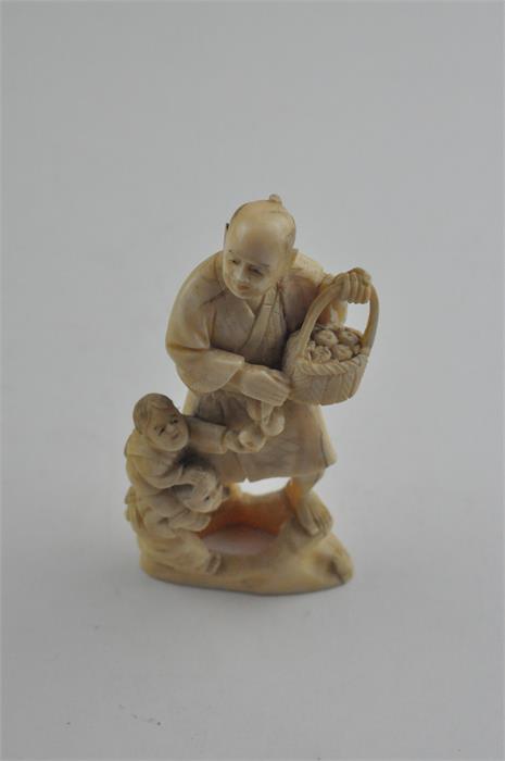 A Japanese Meiji period carved ivory okimono, of a man carrying a basket of fruit with children to