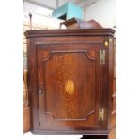 A George III oak hanging corner cupboard, the single panelled inlaid with a paterae roundel,