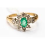 An emerald and diamond flower cluster ring, set with an oval emerald to the centre,