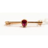 A ruby and unmarked rose gold probably 15ct, small bar brooch, set with a small pear cut ruby,