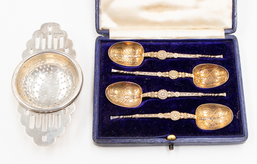 A silver tea strainer and set of four silver spoons (2)