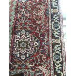 A 20th Century hand knotted woollen runner rug, with symmetrical floral decoration on a red ground,