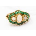 An opal and emerald large dress ring, three oval opals surrounded by a border of round cut emeralds,