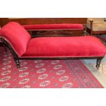 An Edwardian beech framed chaise lounge, upholstered in red, raised on turned legs,