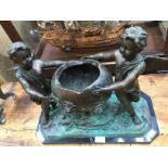 A large unsigned bronze of two cherubs holding a large floral covered cauldron,
