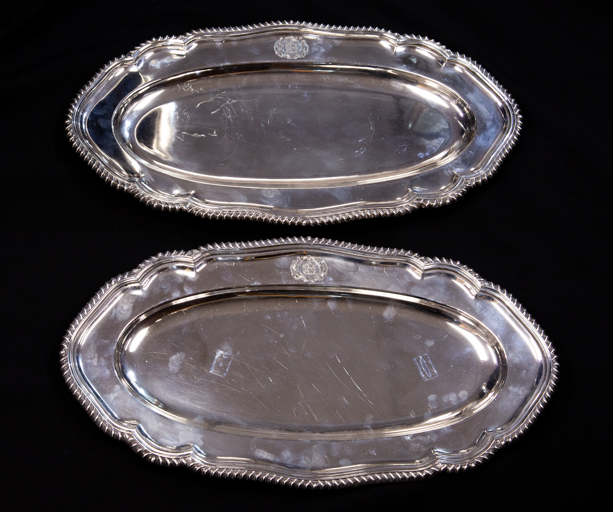 A pair of George V silver platters, elongated oval form, ogee gadrooned borders, with coat of arms,