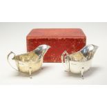 A pair of Edwardian VIII silver sauce boats, each with wavy shaped edges raised on three supports,