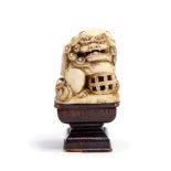 An antique Chinese ivory miniature of A TEMPLE LION CLUTCHING A CAGE, HEIGHT 3.