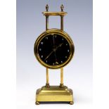 An early 20th Century brass gravity desk timepiece, 10cm circular dial with visible movement,