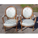 A pair of French giltwood open armchairs, having upholstered oval backs and overstuffed seats,