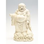 A Chinese blanc de chine figure of Budai, mid 20th Century, standing on a rocky outcrop,