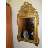 A rectangular wall mirror in a gilt frame, the top with ribbon and flower decoration inset to an