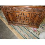 A reproduction oak coffer with hinged lid, carved panelled front, on bun feet - 36in. wide