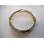 A Chinese green hardstone bangle mounted in 9ct. gold