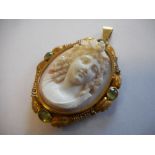 A carved shell cameo mounted in a gold frame with inset green stones as a pendant