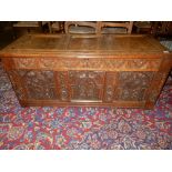 An antique oak coffer with carved hinged lid and panelled front - 51in. wide