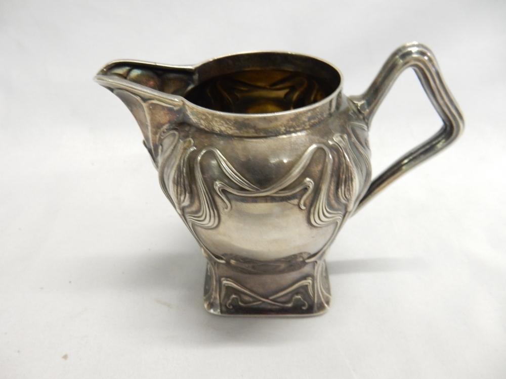 A Russian silver cream jug in the Art Nouveau style with flowers, shaped handle, on square base -