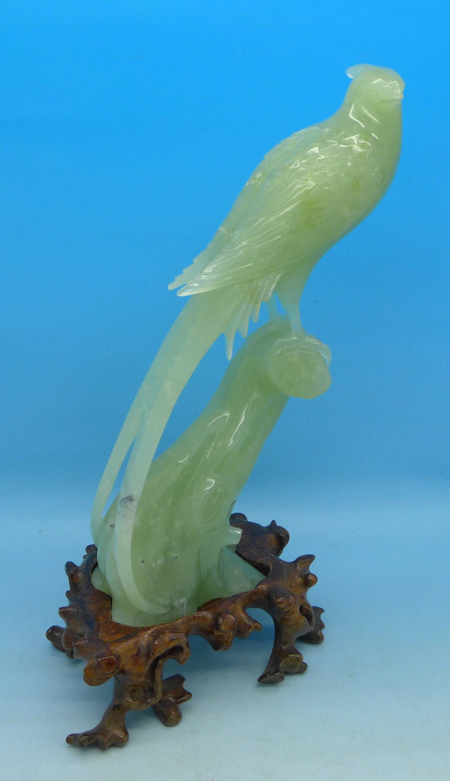 A carved jade model of a bird of paradise on a carved wooden stand, beak a/f,