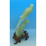 A carved jade model of a bird of paradise on a carved wooden stand, beak a/f,