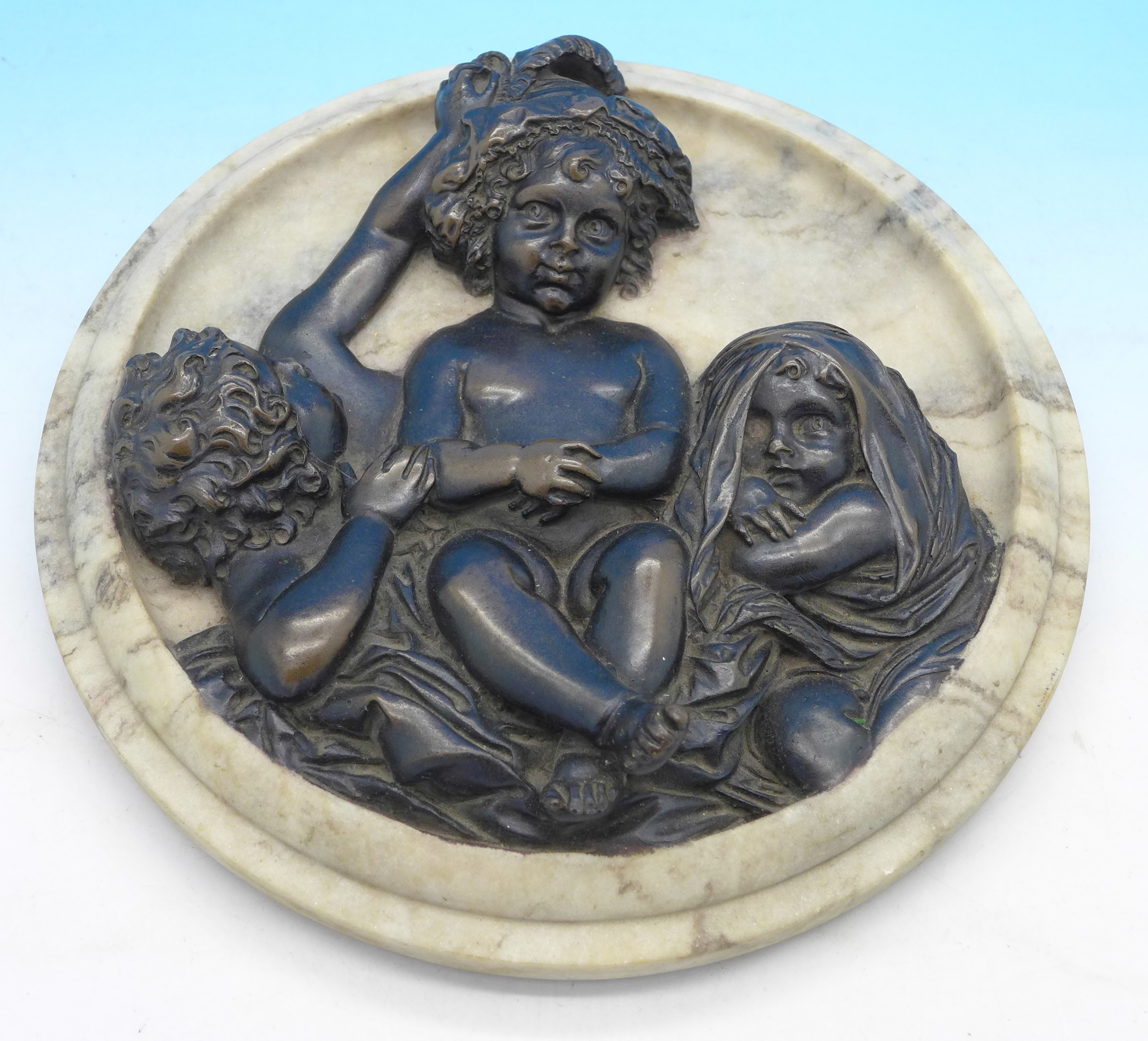 A bronzed plaque depicting three cupids on a reconstituted stone circular surround,