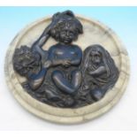 A bronzed plaque depicting three cupids on a reconstituted stone circular surround,