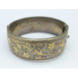A silver bangle with gold applied decoration,