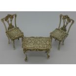 Two silver miniature chairs and a matching table,