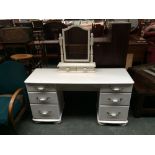 A white dressing table flanked by three drawers with associated adjustable dressing mirror above