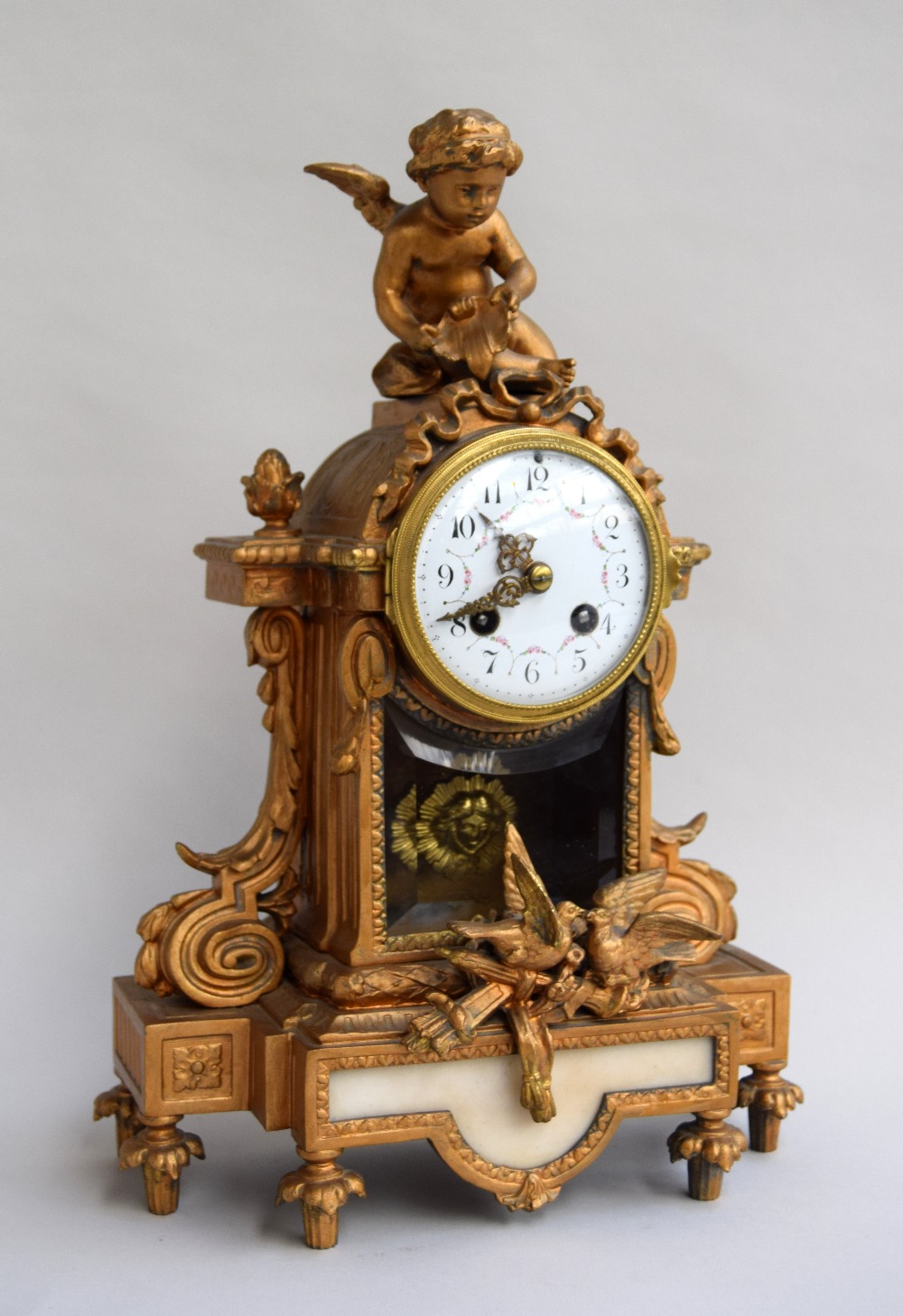 An antique French gilt bronze mantel clock, surmounted by a winged cherub, with two doves to base,