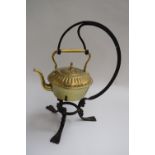 A brass teapot hanging from a wrought iron three legged stand,