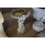 A concrete bird bath raised on figural base