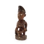 A carved wood African maternity figure, modelled as a female having glass eyes and suckling child,