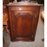 A Georgian oak hanging corner cupboard, enclosed by an arched fielded panelled door, brass hinges