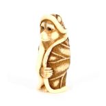 A finely carved Japanese ivory Netsuke, depicting a standing monkey wearing a lily pad hat and gown,