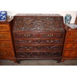 An Antique carved oak bureau, the fall front profusely decorated with cornucopia, flowers and