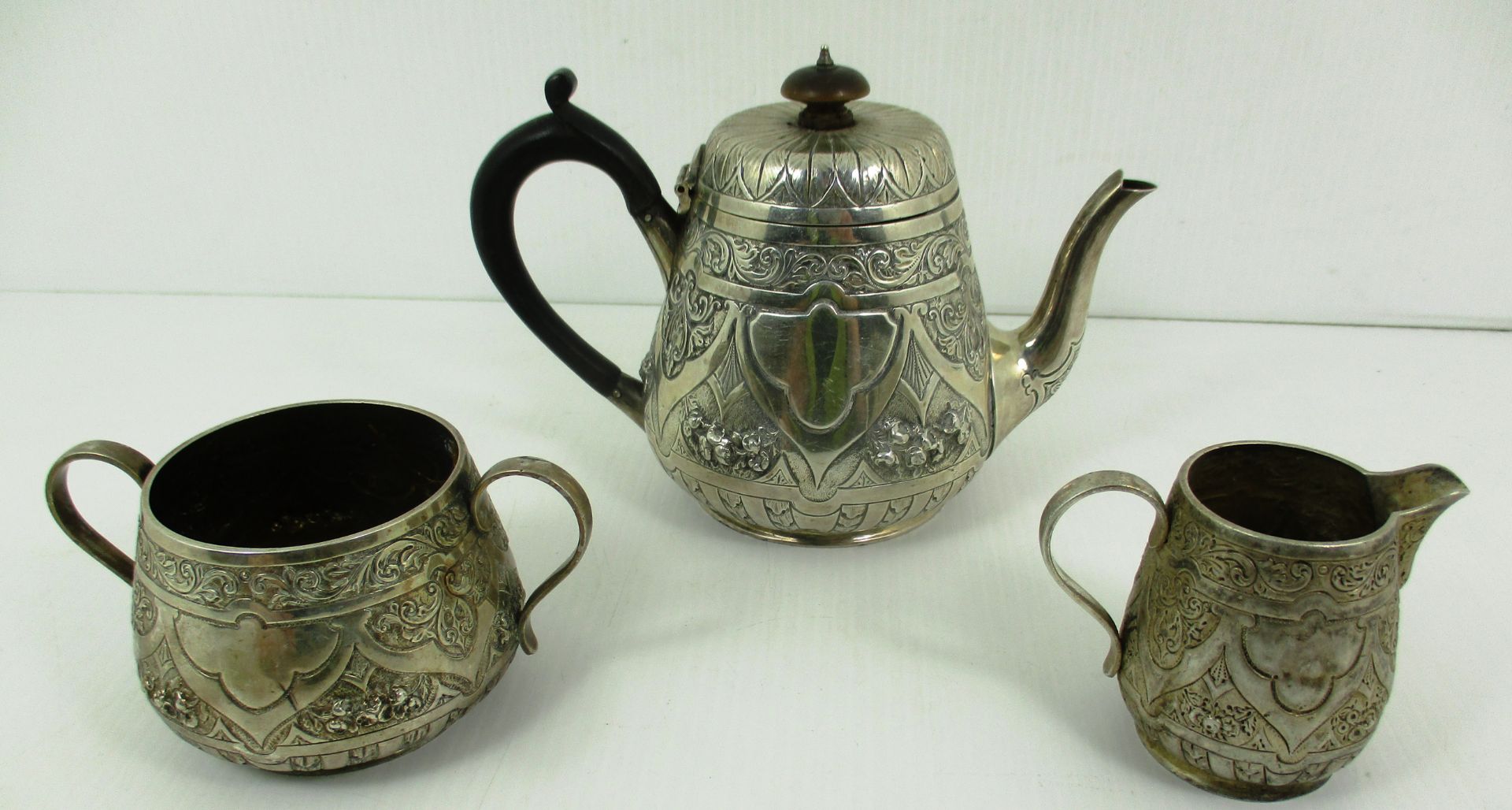 A three piece silver tea set, the teapot with ebonised scroll handle, embossed floral design,