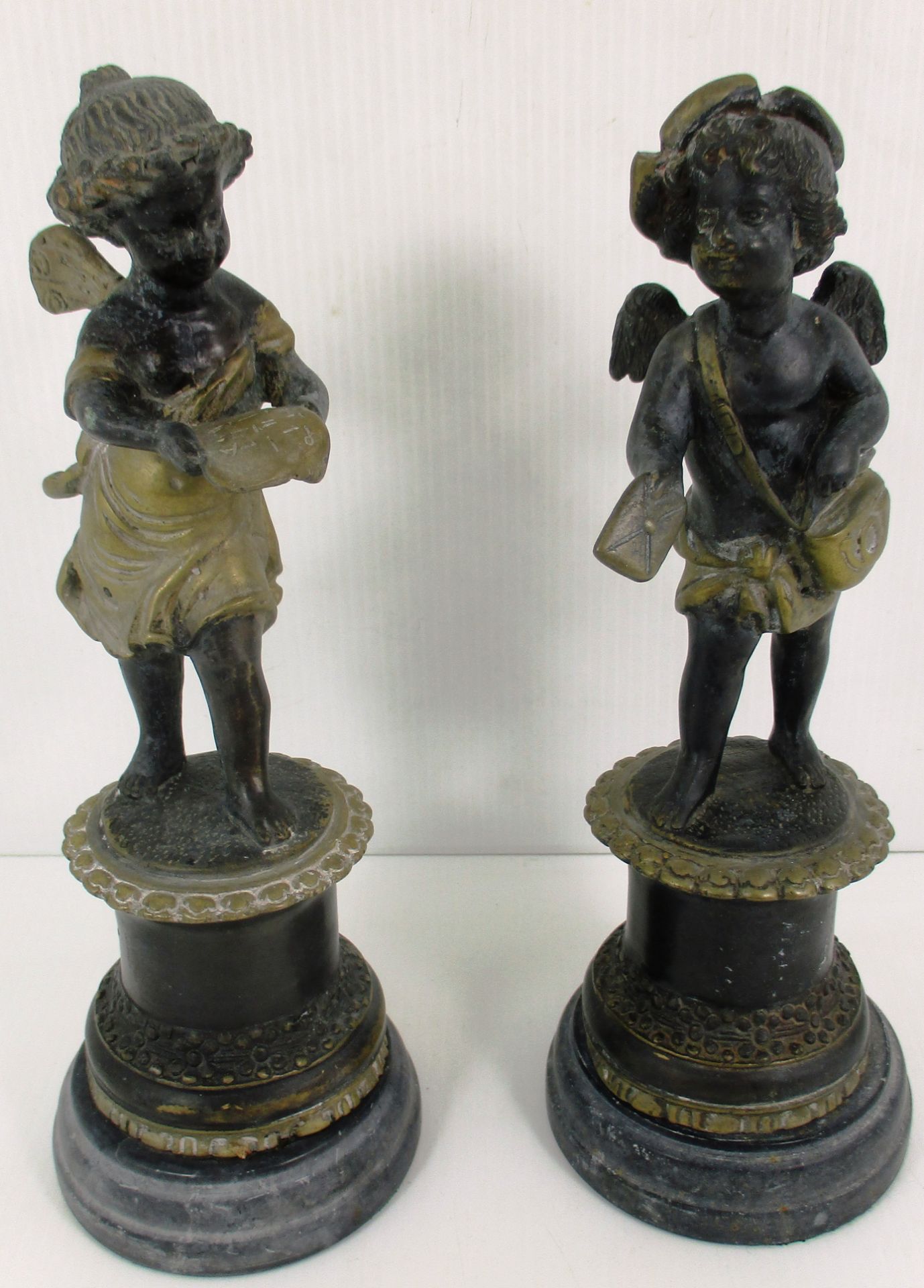 A pair of cast metal cherub figures on faux marble bases