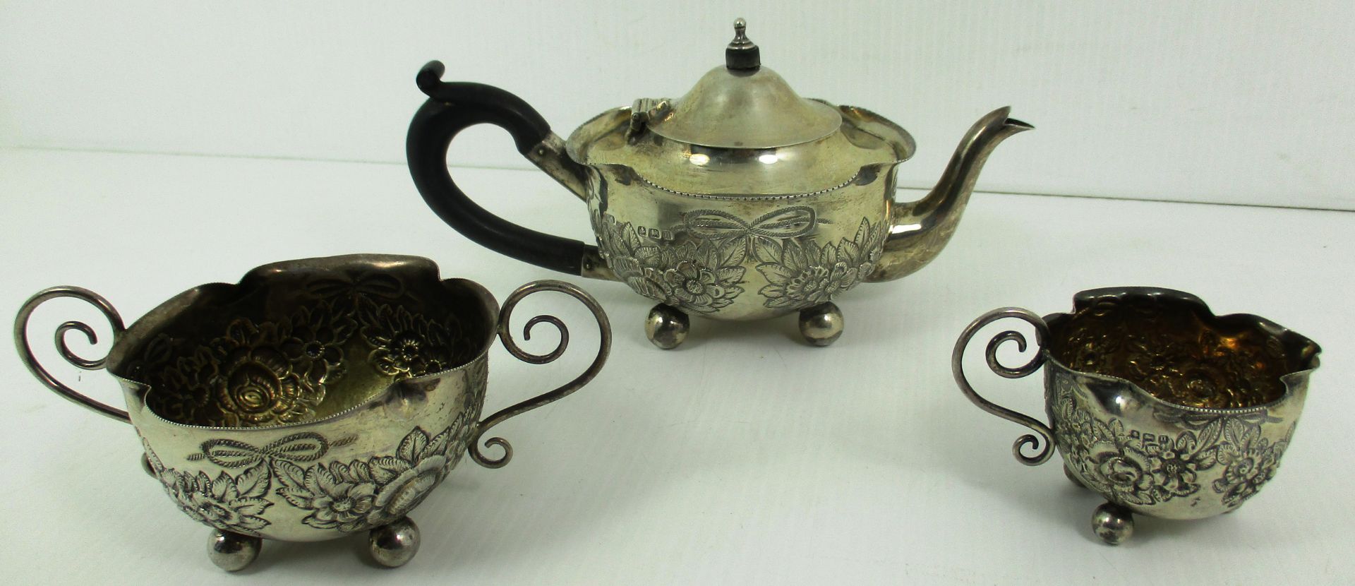 A three piece silver tea set, the teapot with flared rim, ebonised scroll handle,