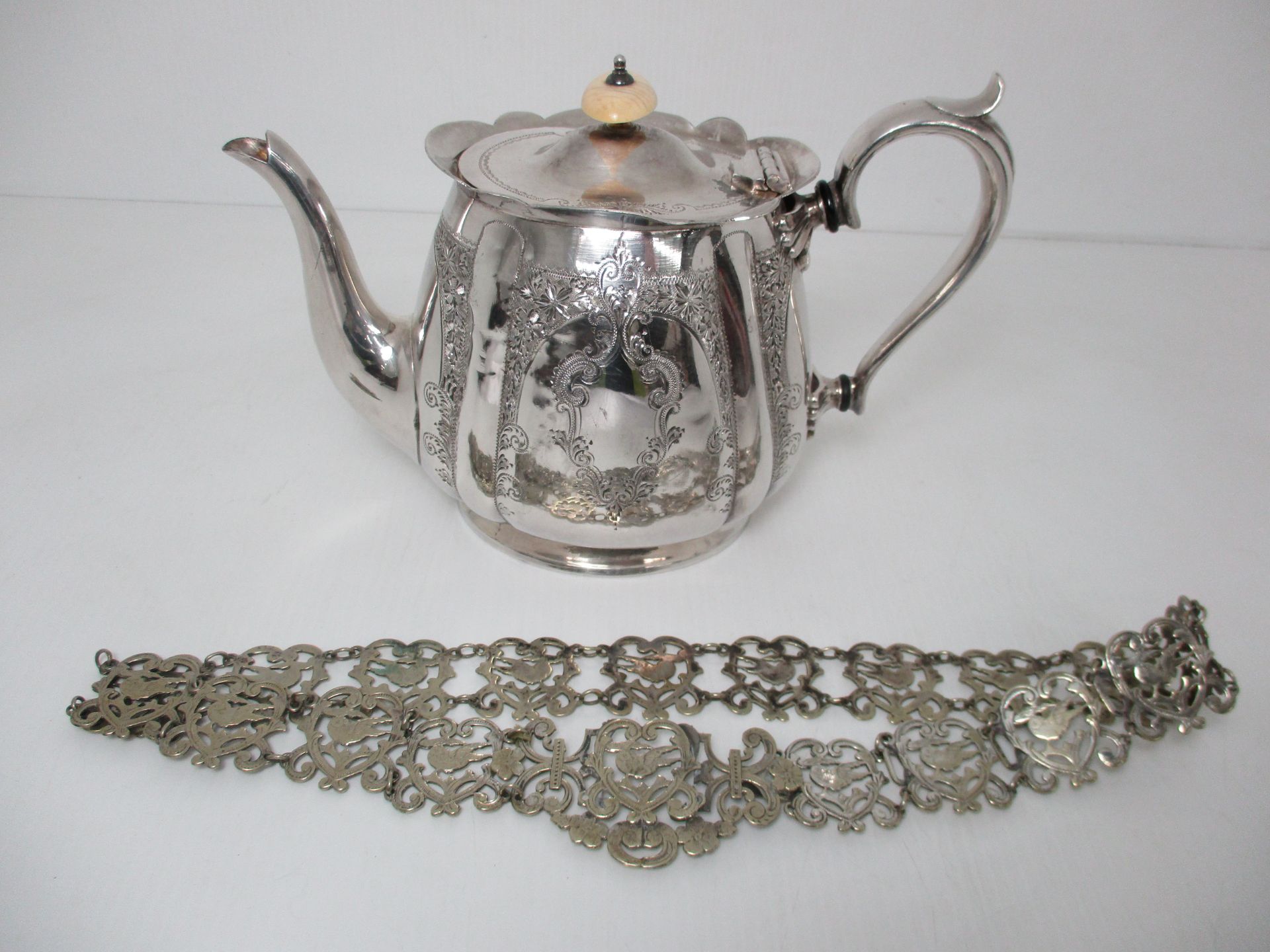 A silver plated teapot with scroll handle and heavily engraved design and a silver plated ornate