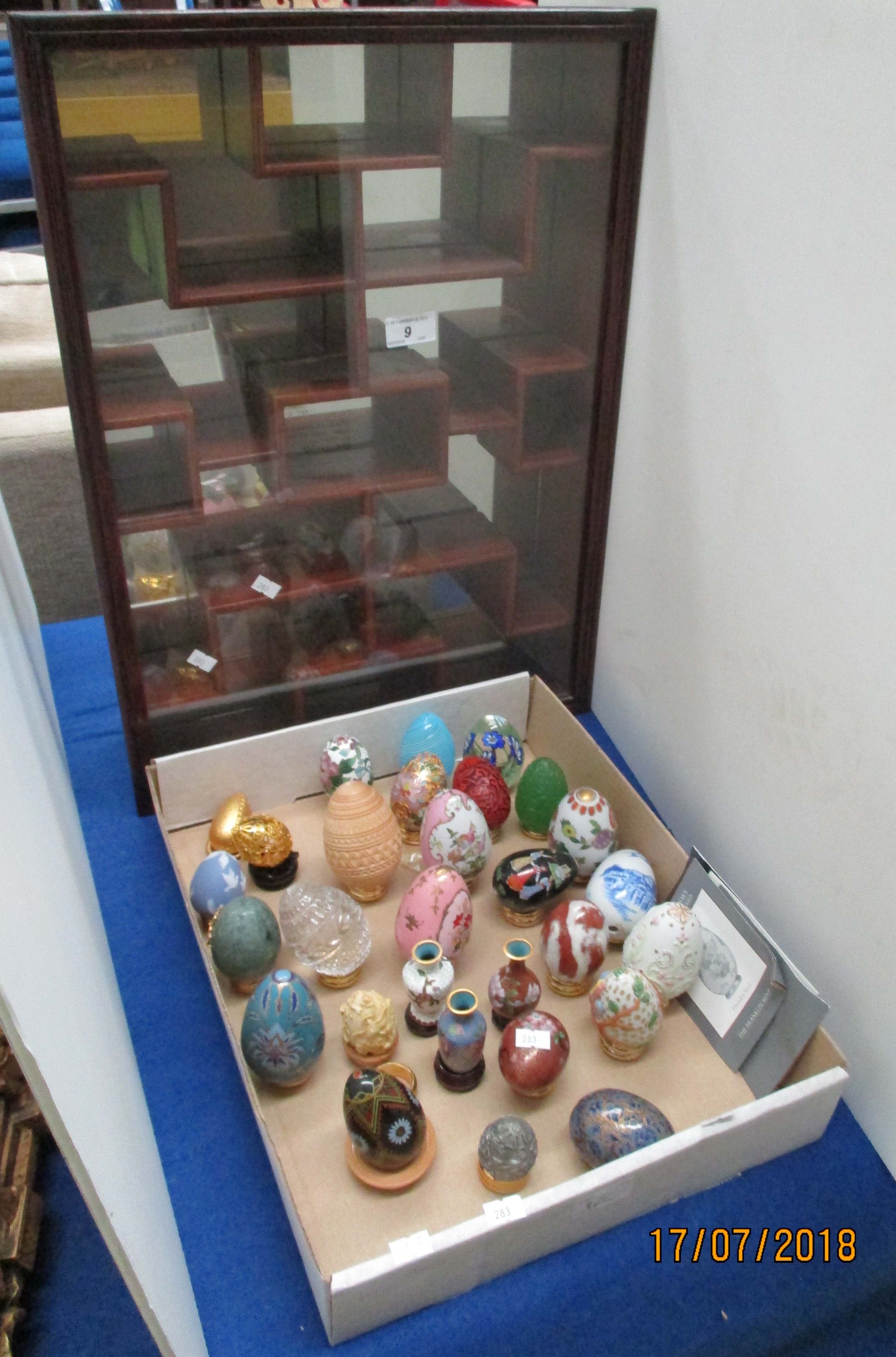 A mahogany finish glass front wall cabinet enclosing a collection of decorative treasury eggs and