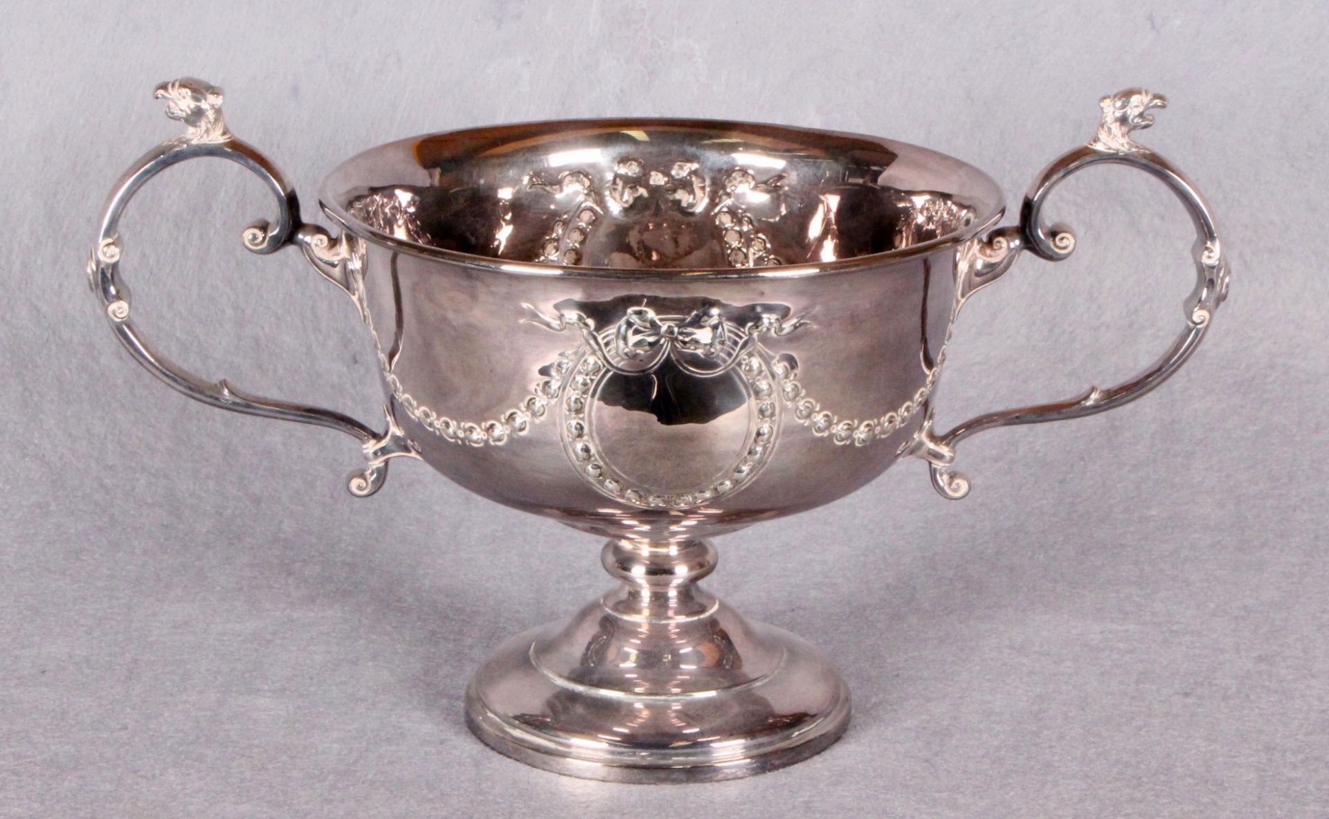 A two-handled pedestal rose bowl, repoussé with swags of ribbon tied floral branches, circular base,