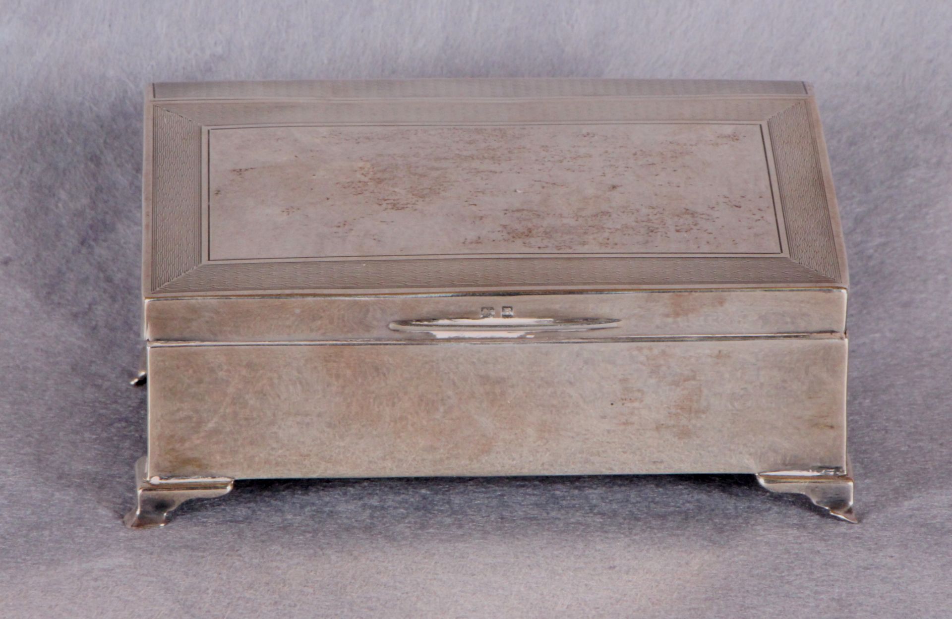 An engine-turned silver cigarette box with hinged, sloping lid, cedar lining,