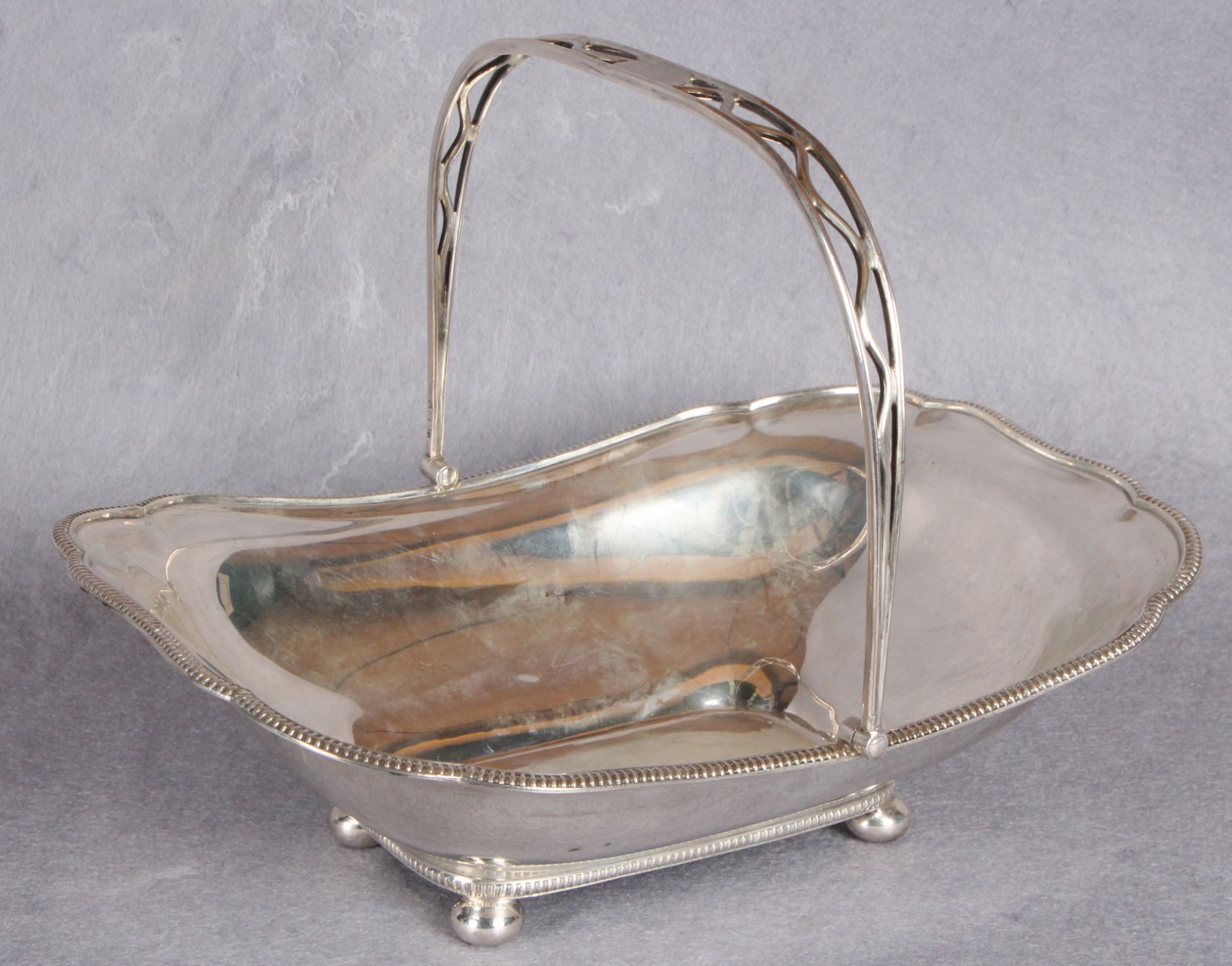 A shaped rectangular cake basket with swing handle, four ball feet,