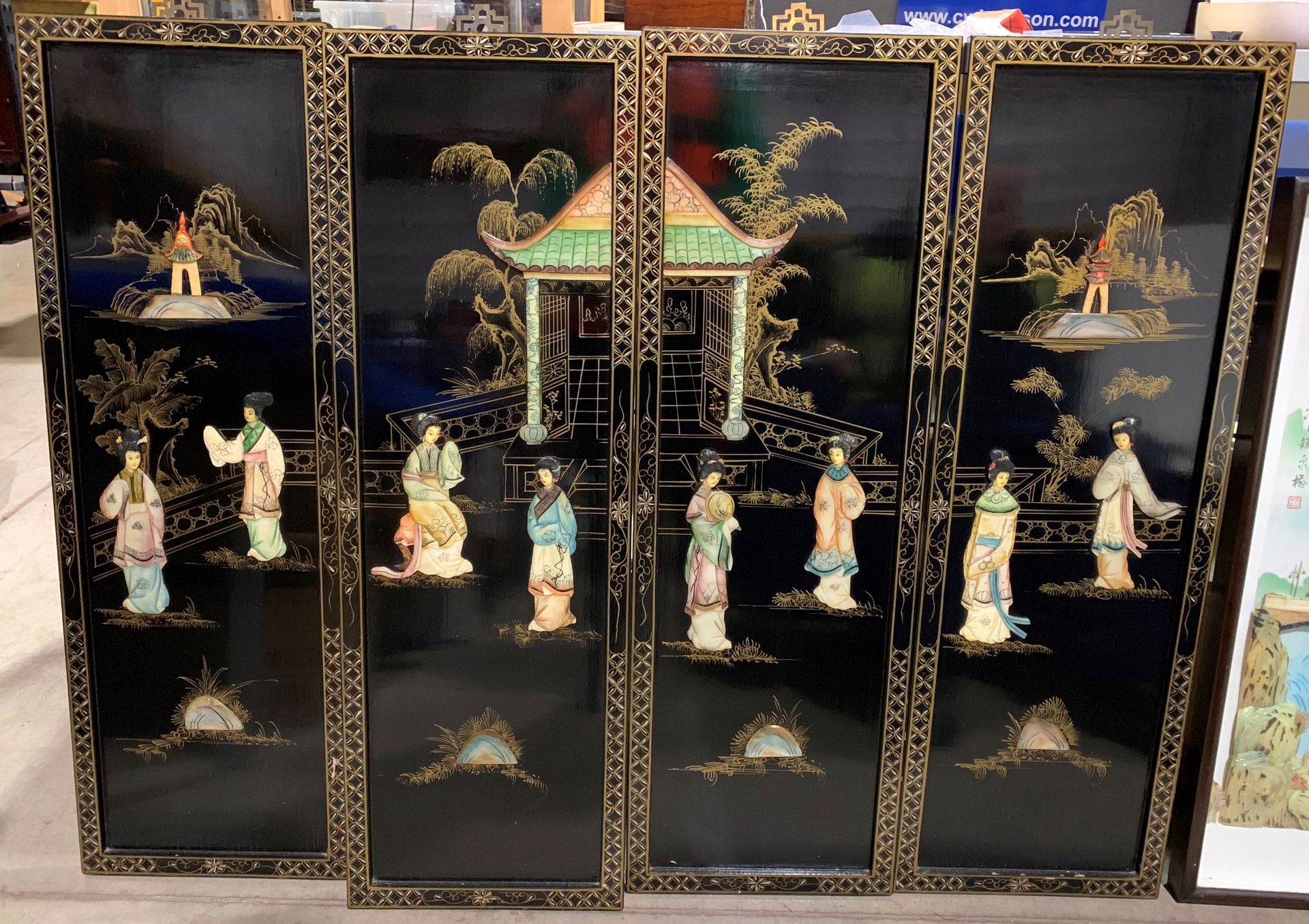 A set of four ebonised Oriental panels depicting life outside the temple,