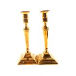 A pair of late 18th Century Adam style brass candlesticks on stepped square bases,