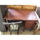 A stained oak three drawer desk with a folding leaf and an upholstered stick back chair