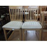 A set of four light wood dining chairs with cream upholstered seats