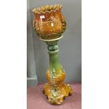 A green and brown ground pottery jardiniere on stand, indistinct signature to jardiniere,